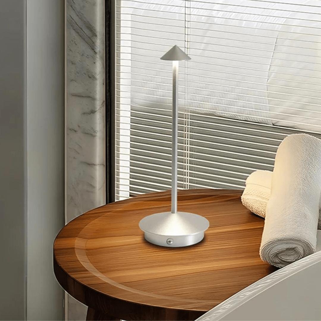 Silver lamp on a wooden nightstand with a blurred window background