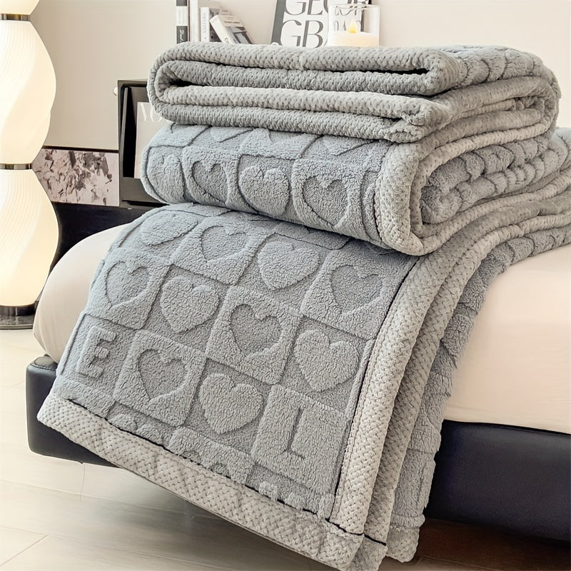 Gray textured blanket with heart pattern draped over a bed in a bedroom setting.