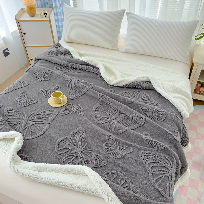 Gray butterfly-patterned blanket on a bed with white pillows and a small table in the background.