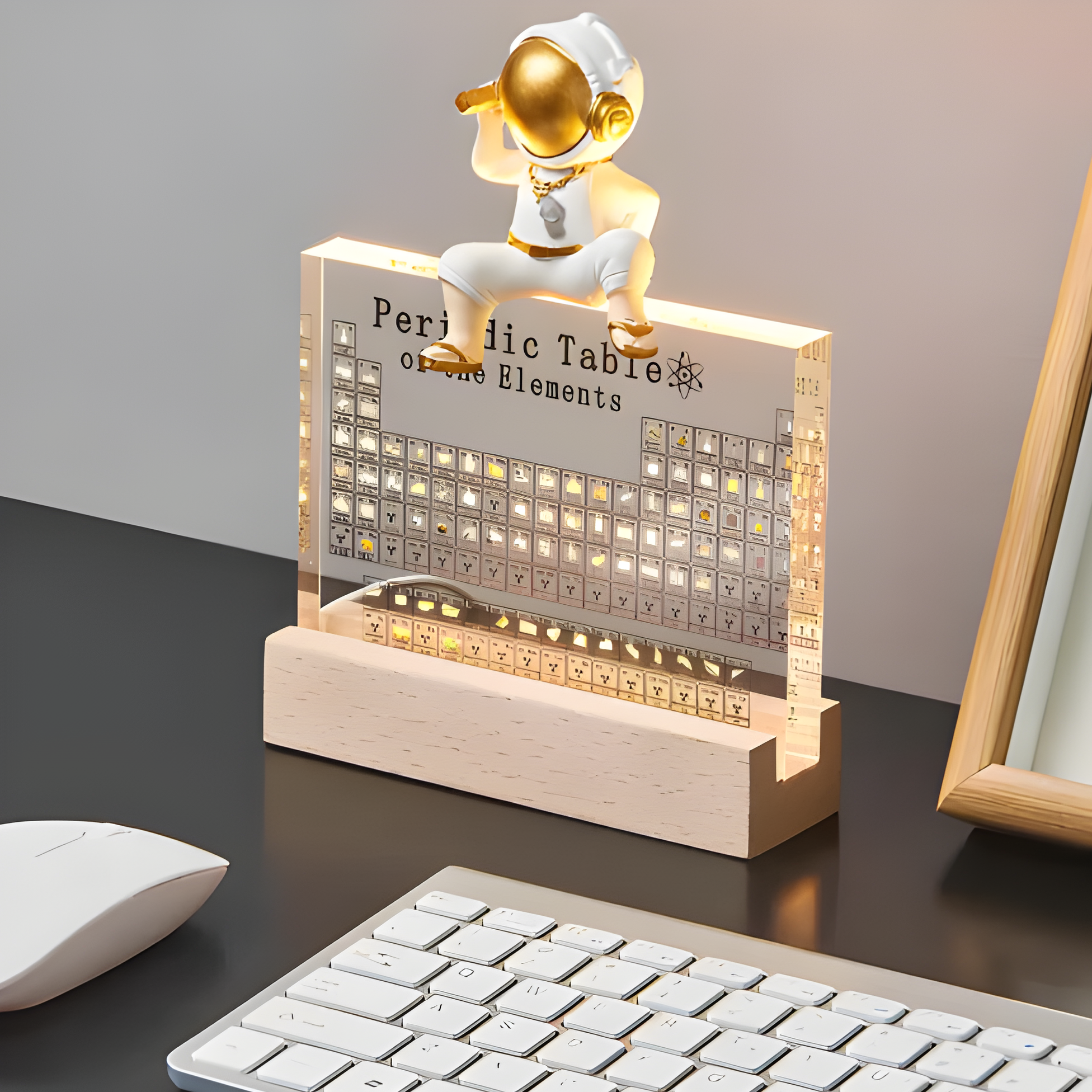 Decorative periodic table lamp with a small figure on top, placed on a desk with a keyboard and mouse.