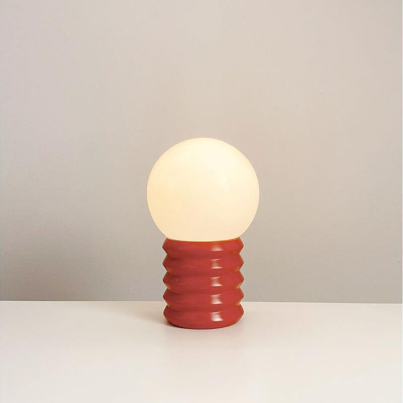 Small lamp with a red base and white bulb on a neutral background