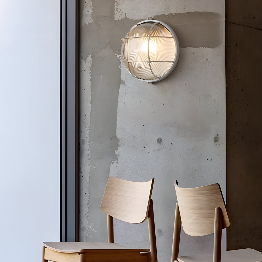 Round wall light fixture on a textured wall with wooden chairs below.