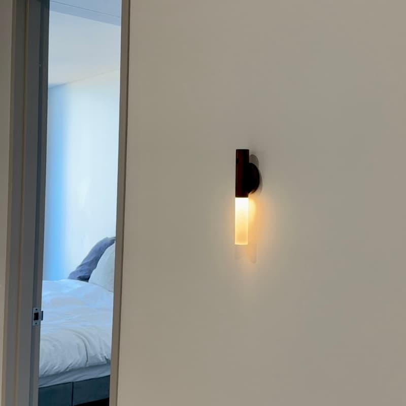 Wall-mounted light fixture on a white wall with a bedroom visible through an open door.