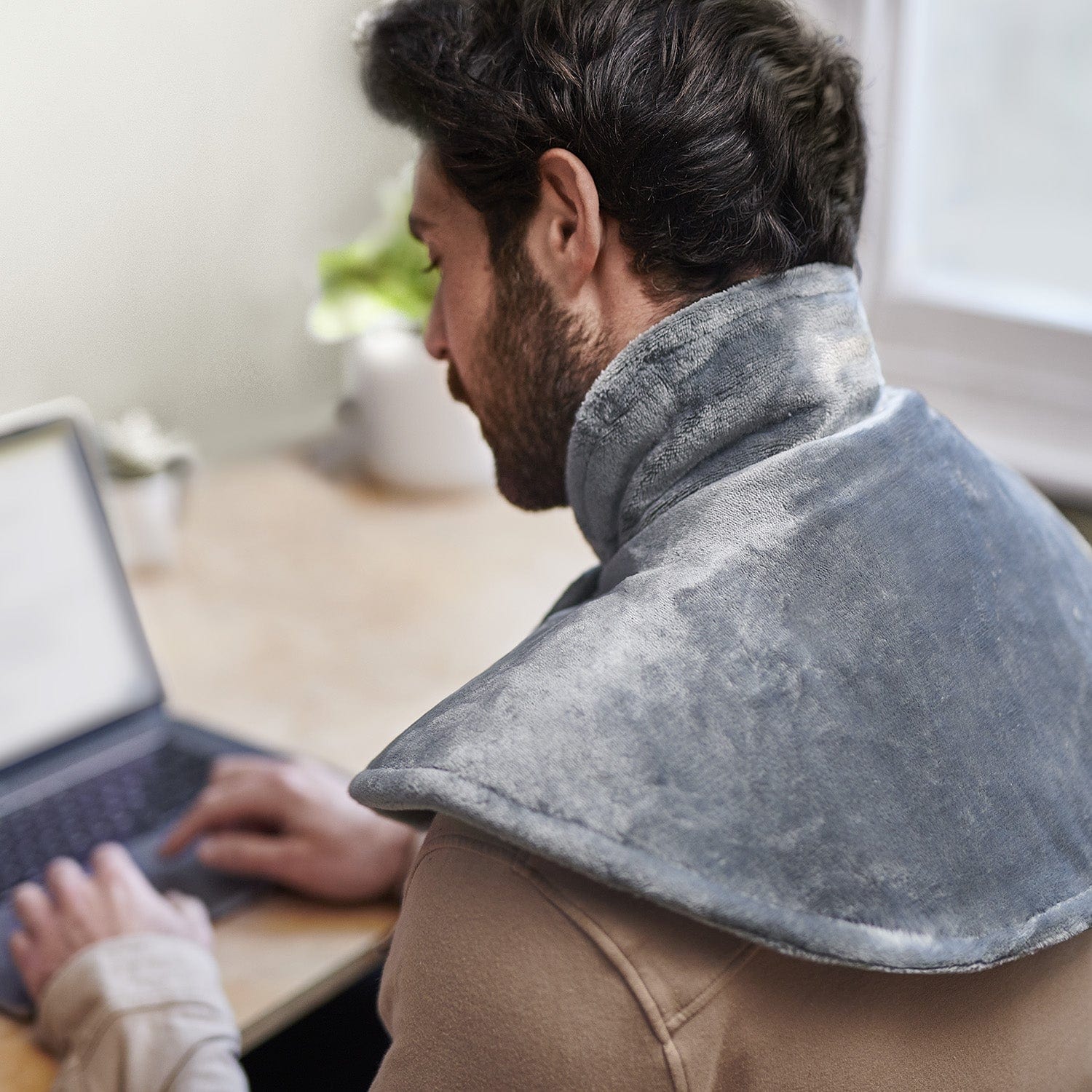 Person using a laptop with a neck pillow on their shoulders