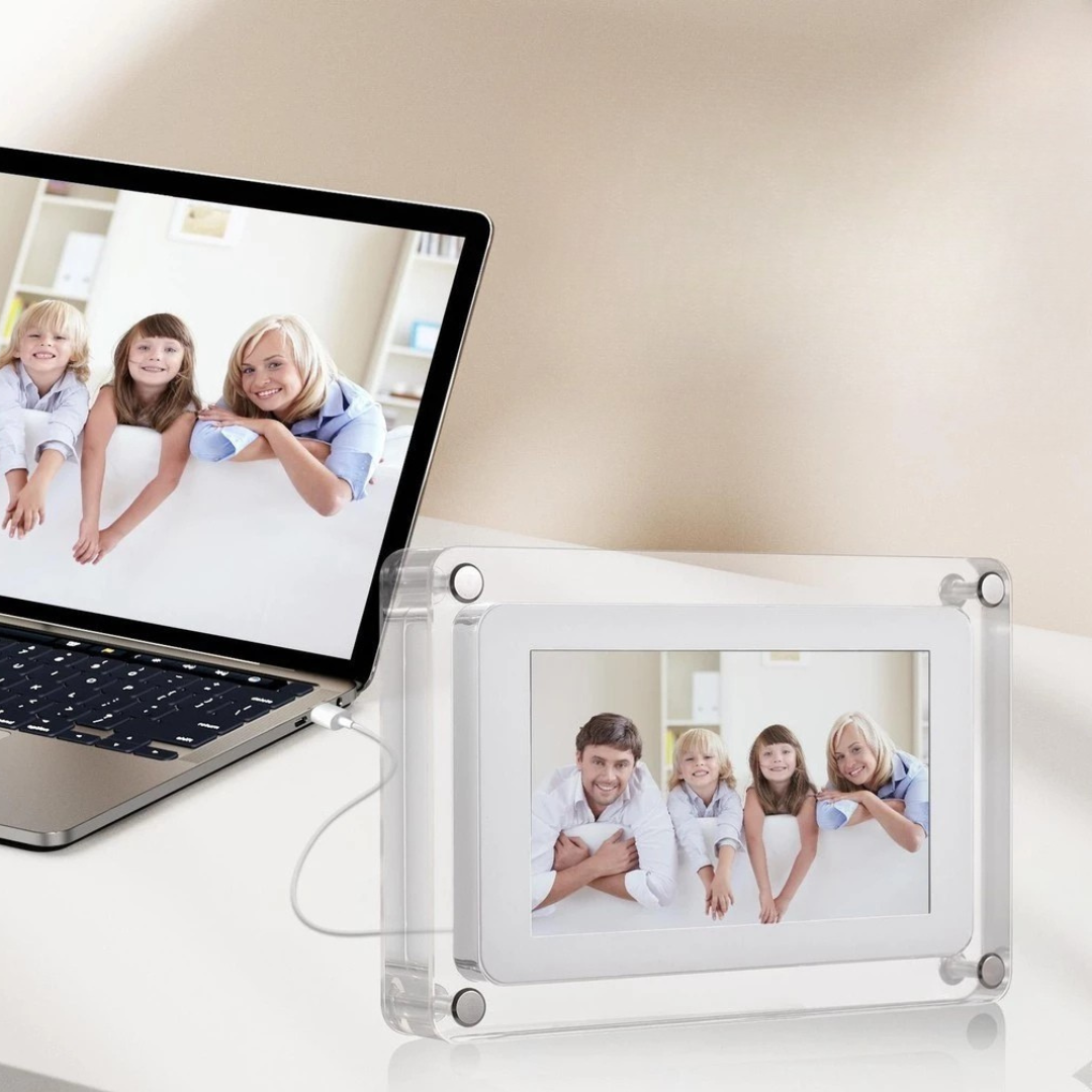 Digital photo frame displaying a family photo next to a laptop on a light surface.