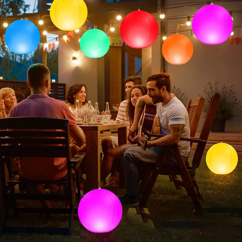 Group of people sitting around a table with colorful floating lights in an outdoor setting.