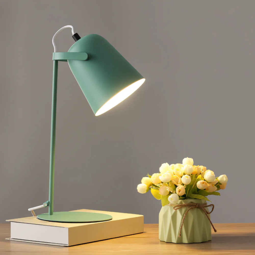 Green desk lamp on a wooden surface with a small vase of flowers.
