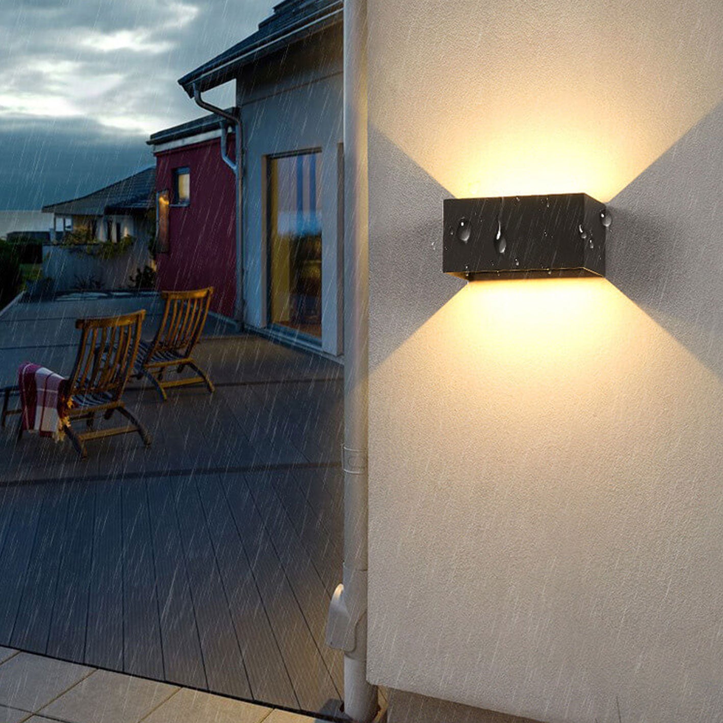 Outdoor wall light fixture on a house exterior with a patio and chairs in the background.