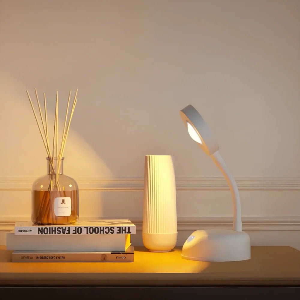 White desk lamp on a wooden surface with books, a vase, and a diffuser.