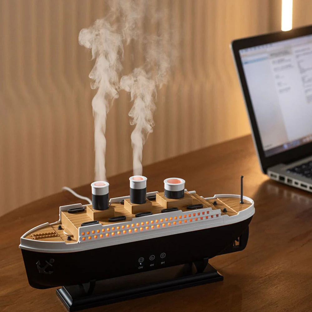 Model of a ship with smokestacks on a wooden surface next to a laptop.