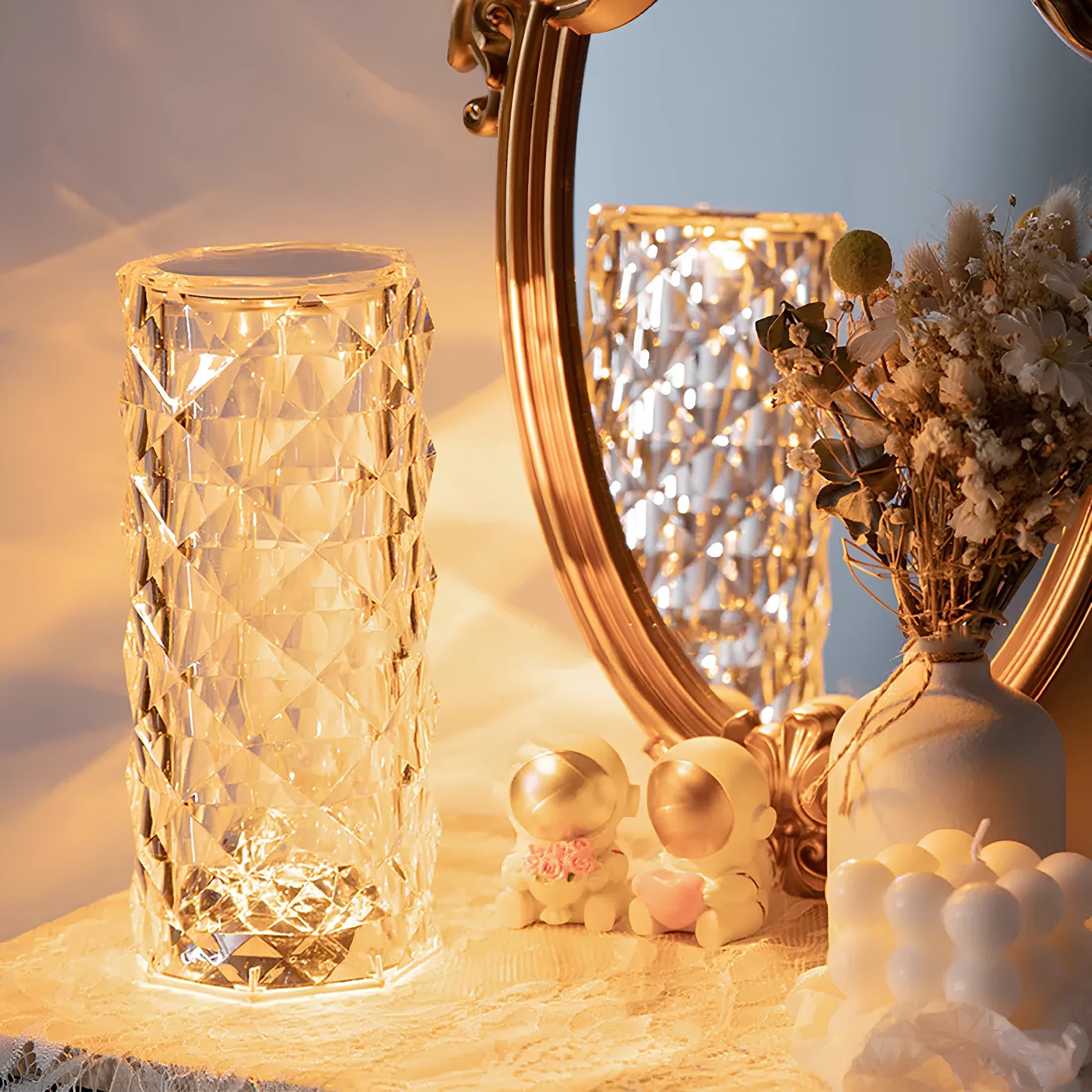 Decorative scene with a textured glass vase, small figurines, and a mirror on a surface.