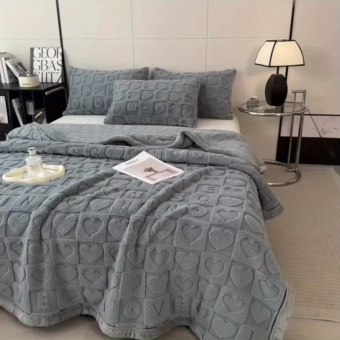 Gray textured bedspread on a bed in a bedroom setting with a lamp and books in the background.