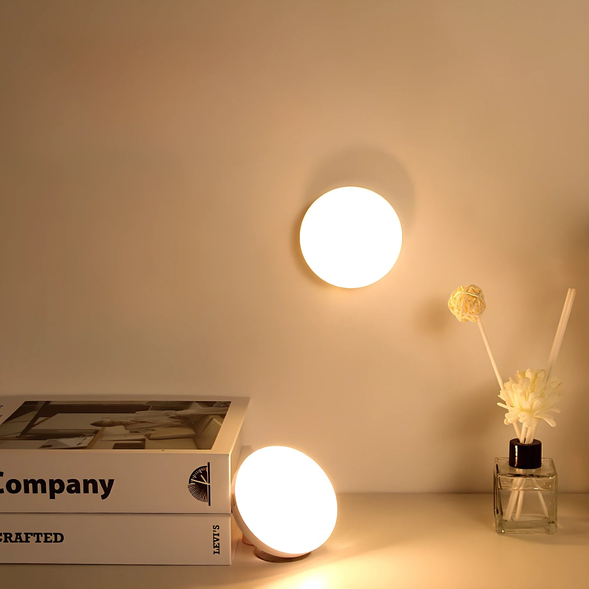 Round wall-mounted light fixture on a neutral wall with books and a vase in the foreground.