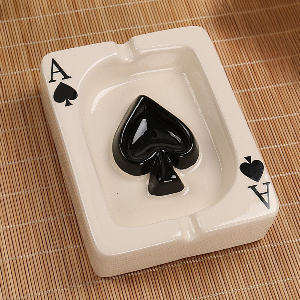 Ceramic ashtray shaped like a playing card with an ace of spades design on a woven mat background.