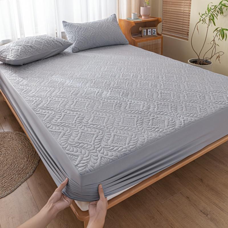 Person unfolding a gray mattress protector on a bed in a bedroom.