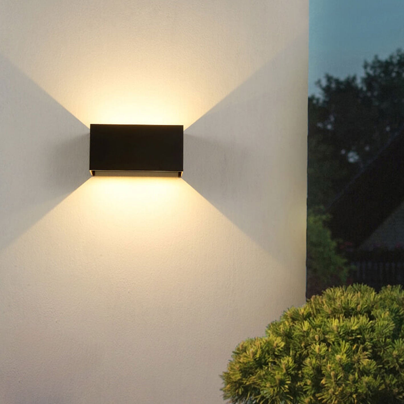 Modern outdoor wall light fixture on a building exterior with a tree in the background.