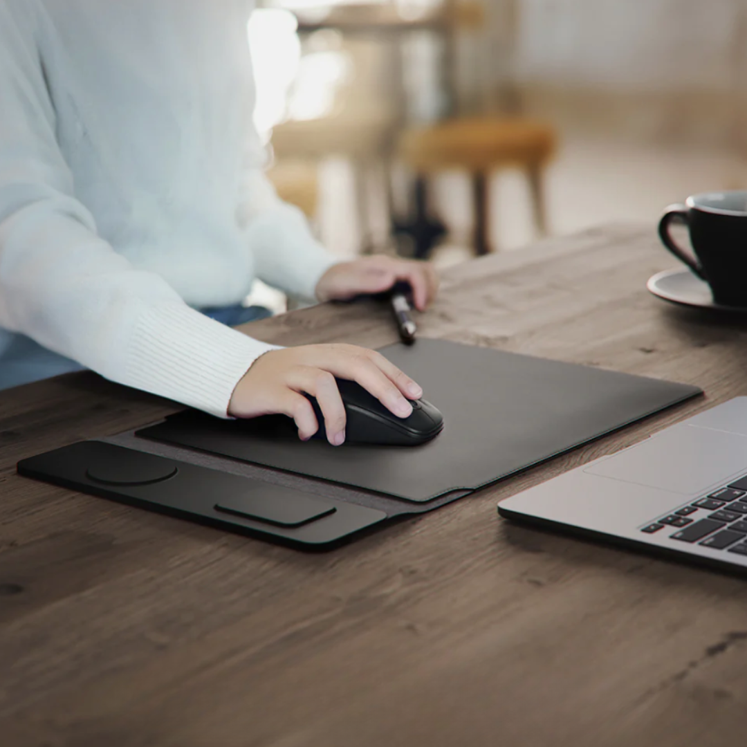 Person using a computer mouse on a desk with a laptop and coffee cup in the background
