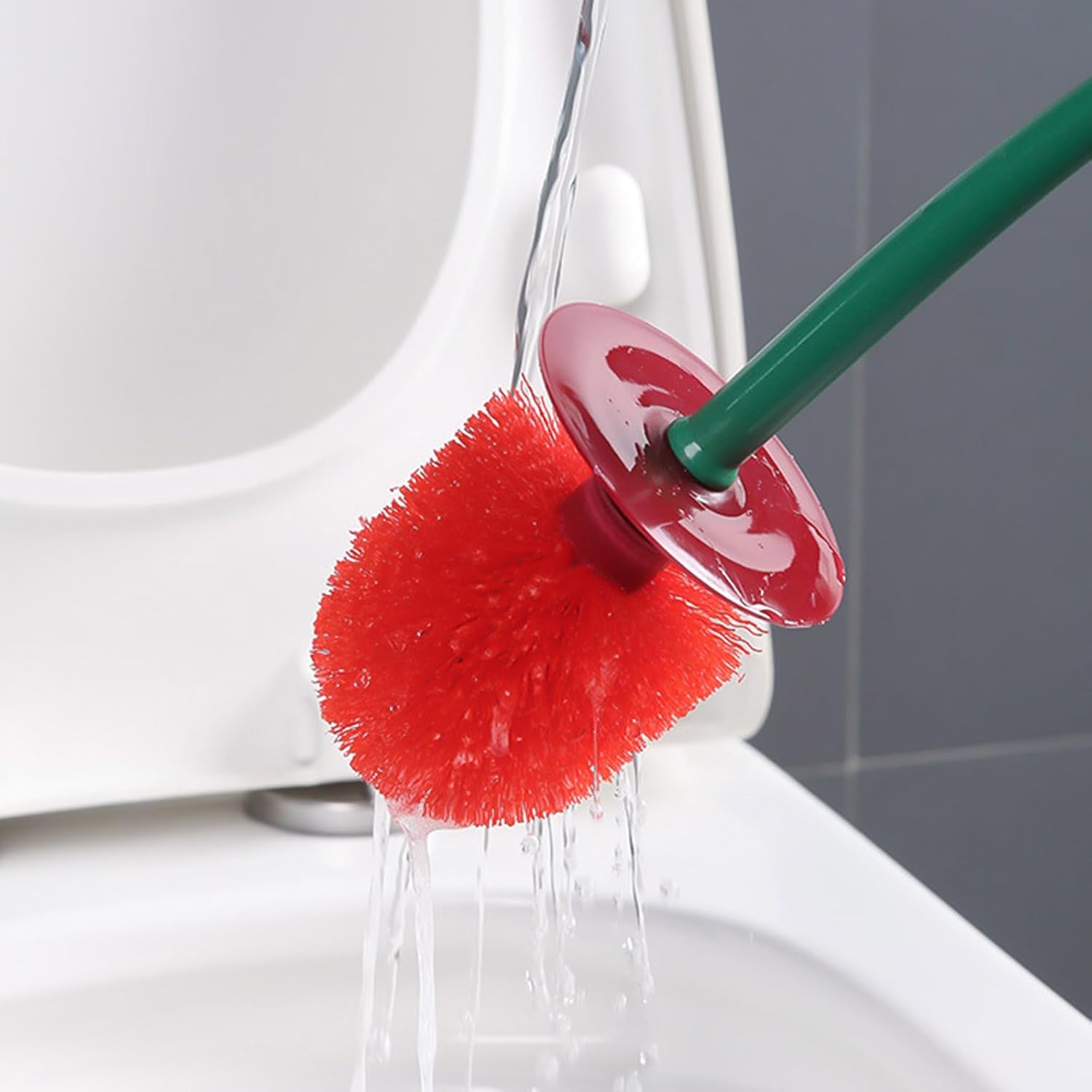 Red scrubber with a green handle cleaning a white toilet bowl.