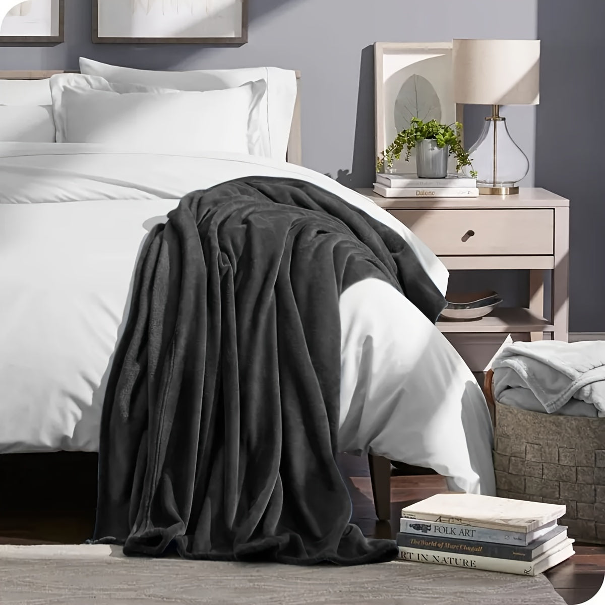 Gray blanket draped over a bed in a bedroom setting with a nightstand and books.