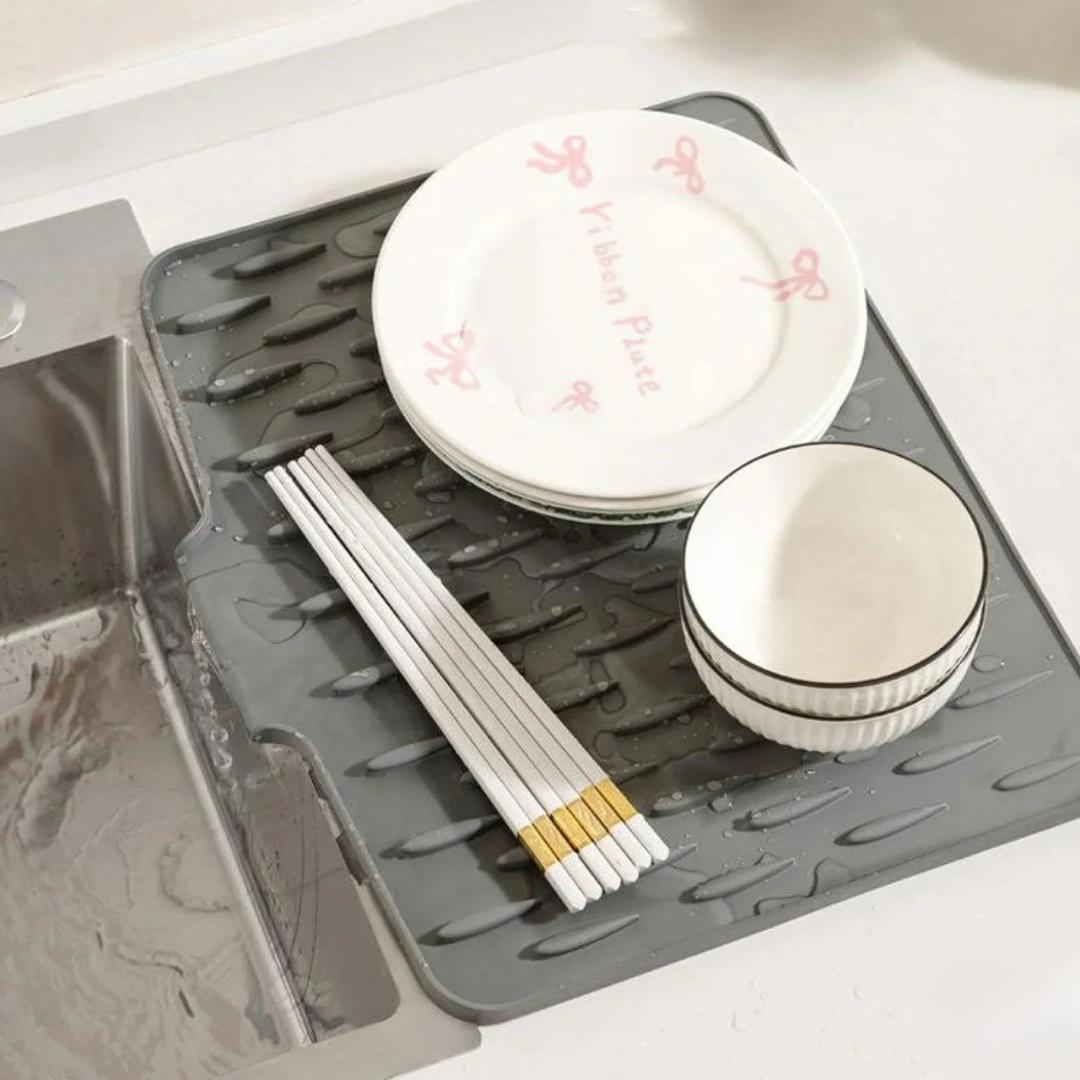 Gray dish drying mat with plates, bowls, and chopsticks on a kitchen counter.