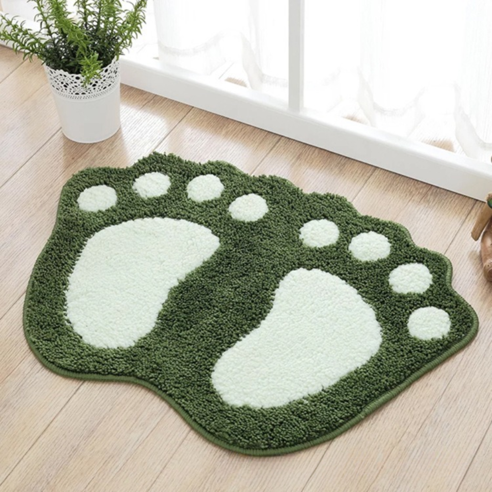 Green and white foot-shaped rug on a wooden floor with a plant in the background.