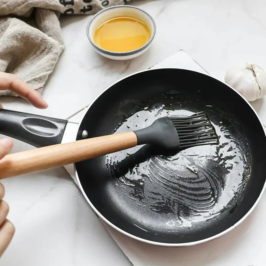 Person using a brush to apply oil to a frying pan on a white surface.