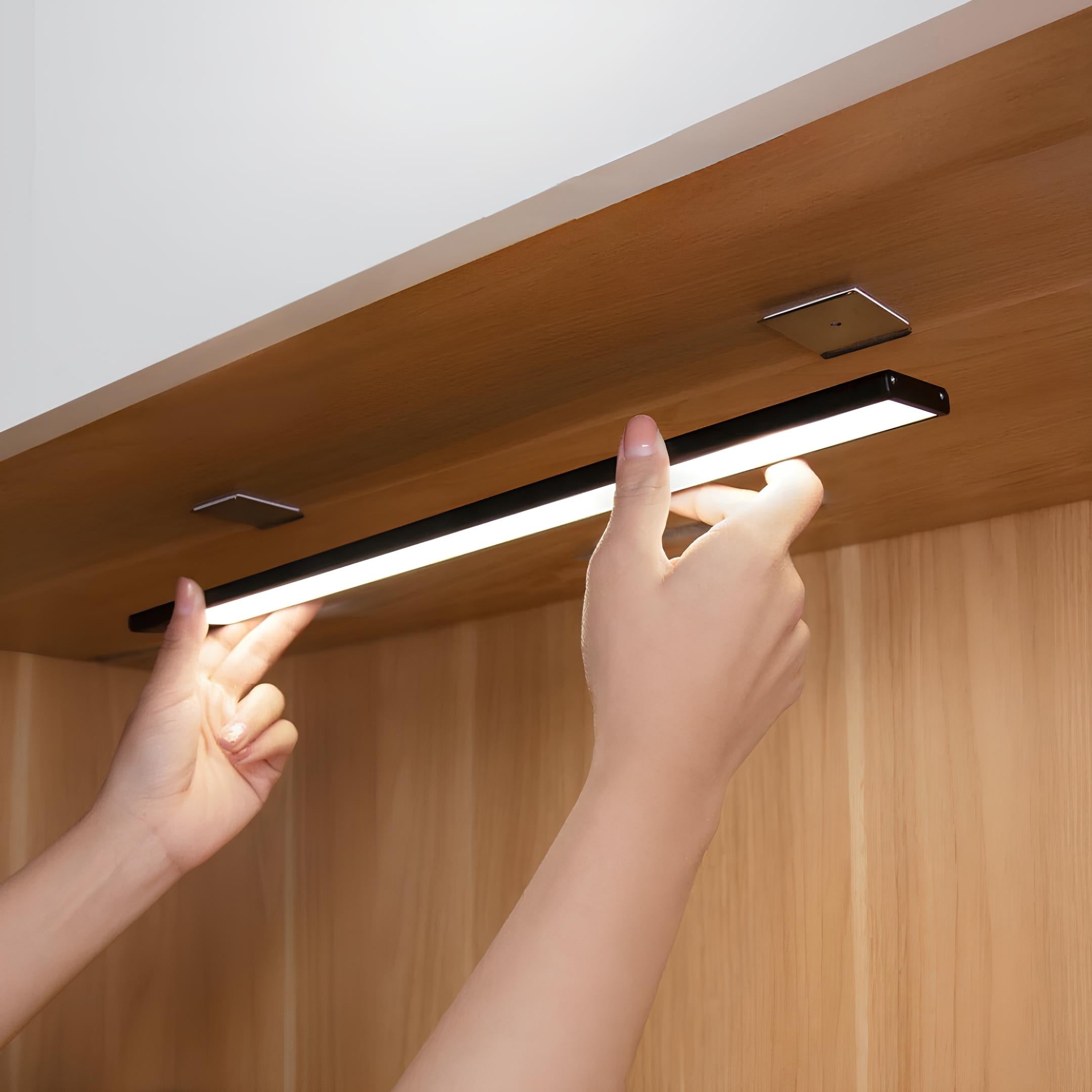 Person adjusting a strip light under a wooden cabinet.