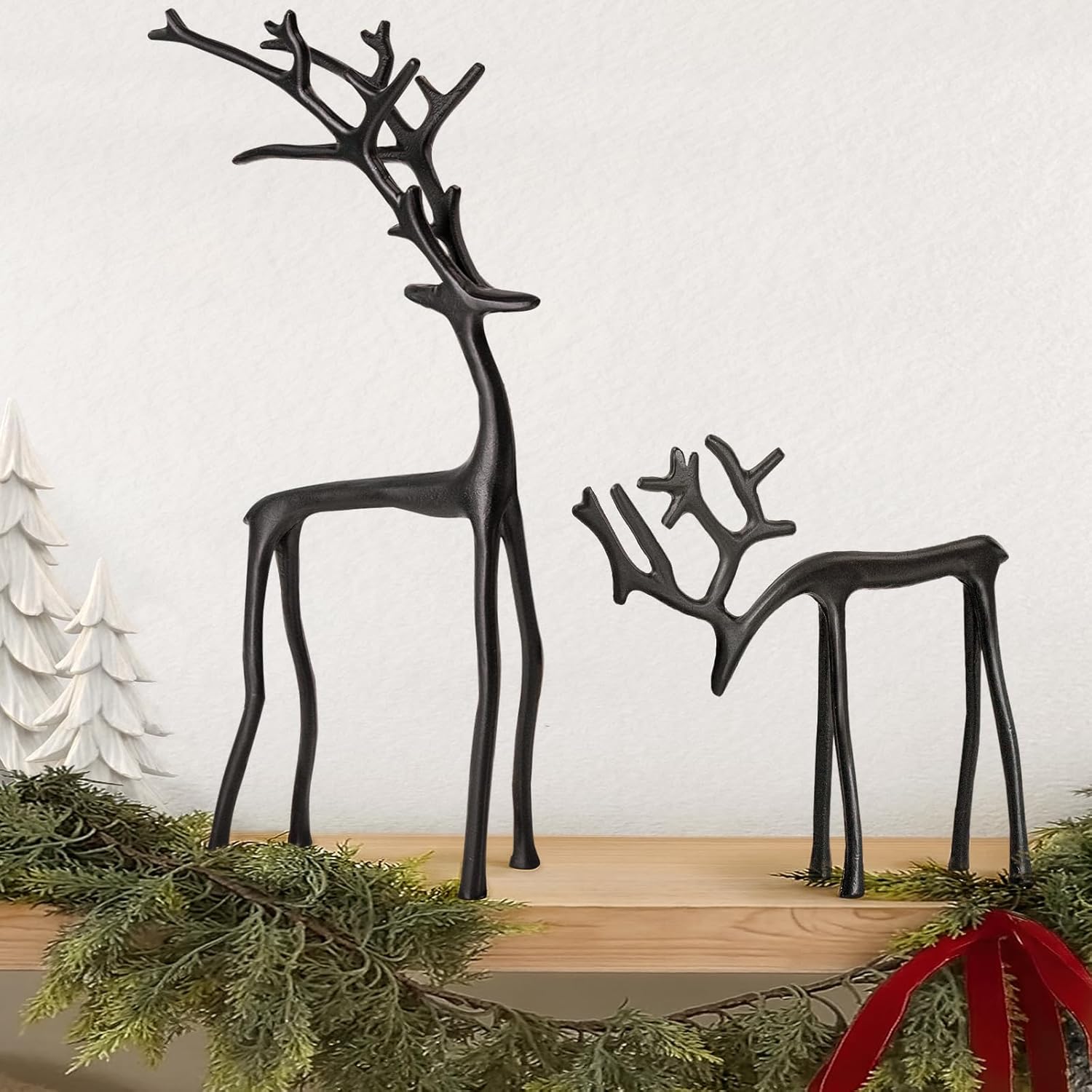Decorative black reindeer figures on a wooden surface with greenery and a white background