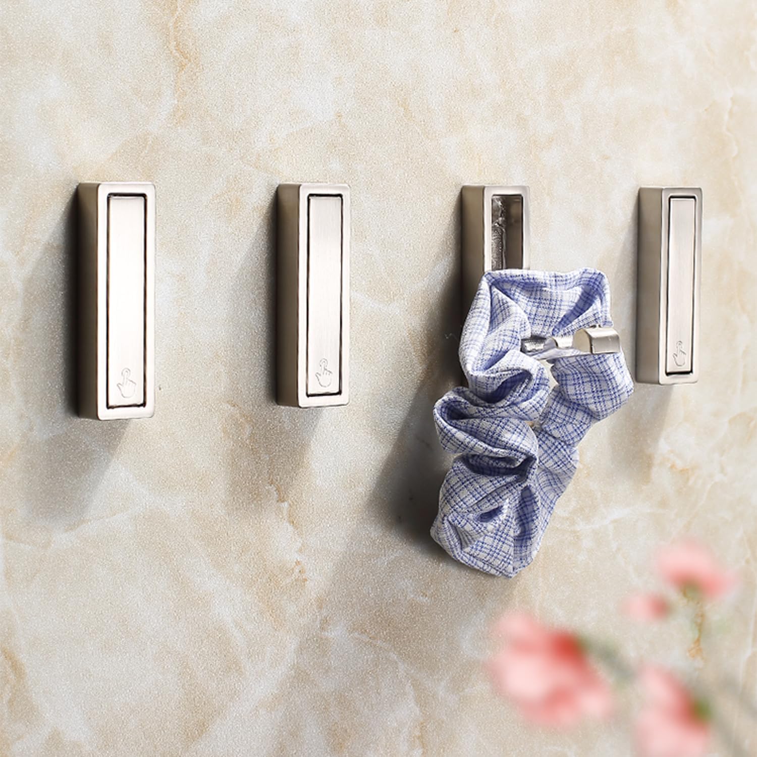 Set of four metal wall hooks on a textured beige wall with a blue and white checkered cloth hanging on one of them.