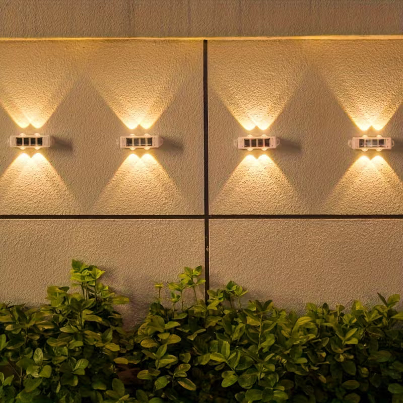 Wall-mounted outdoor lights on a textured wall with greenery at the bottom.