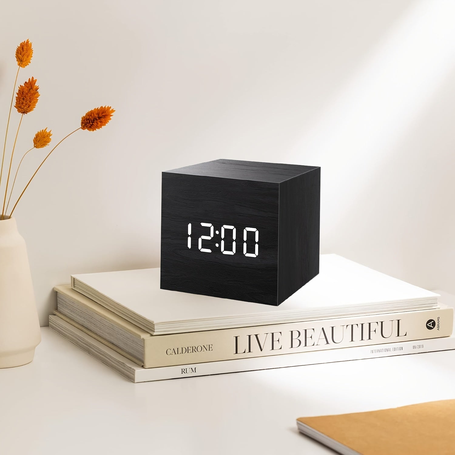 Black digital clock on a stack of books with a vase of flowers in the background