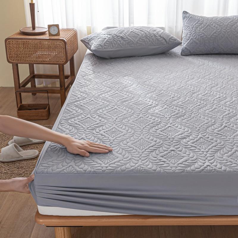 Person adjusting a gray quilted mattress cover on a bed in a bedroom.