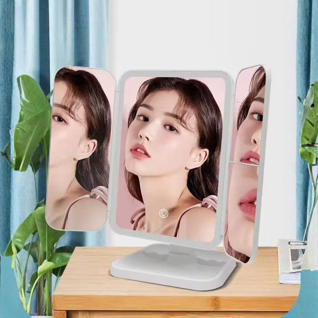 Makeup mirror with multiple angles of a person's face on a wooden table with plants in the background.