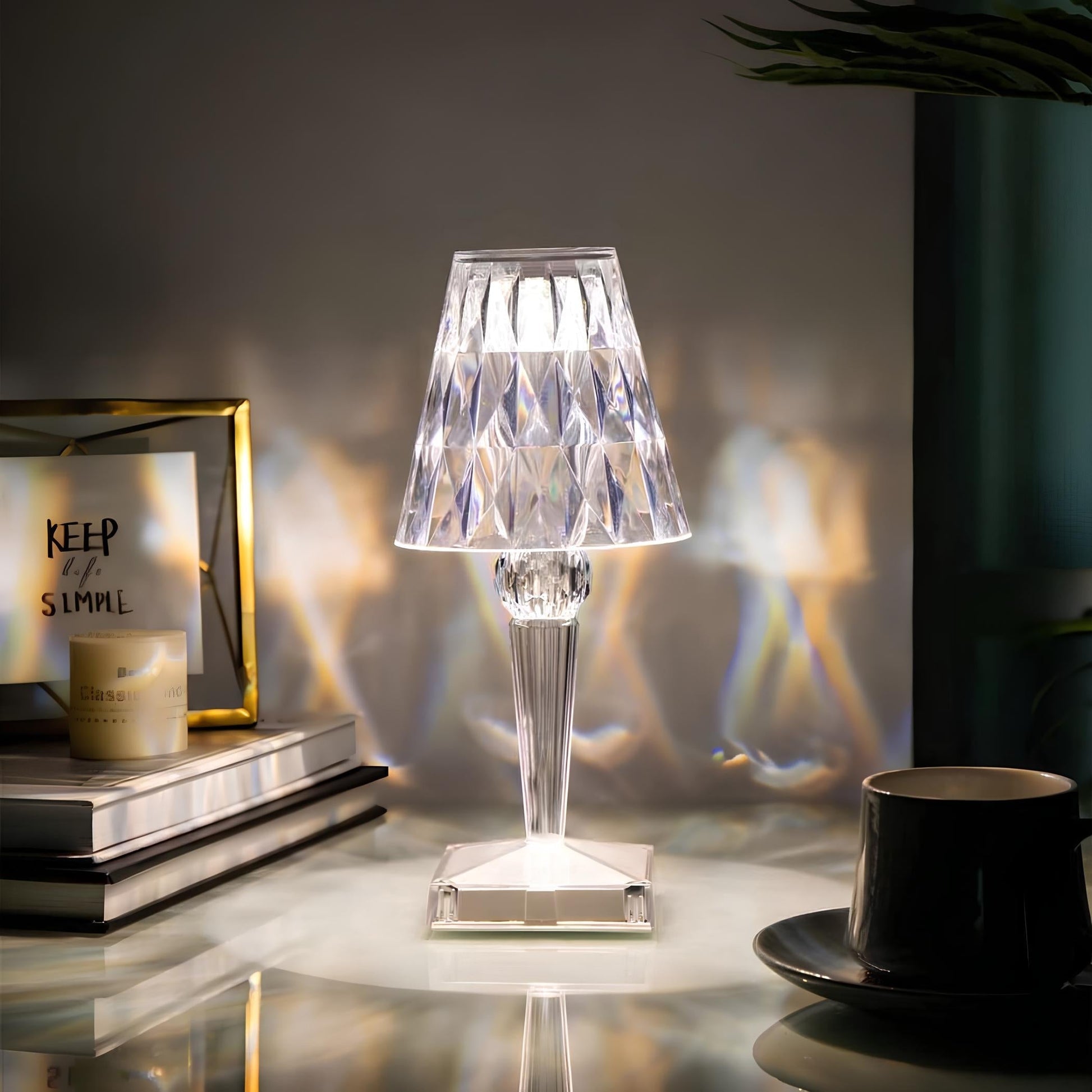 Crystal table lamp on a reflective surface with books and a cup in the background