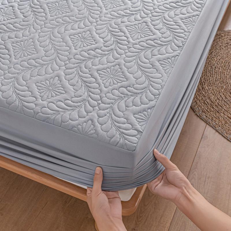 Person holding a gray mattress protector on a wooden bed frame.