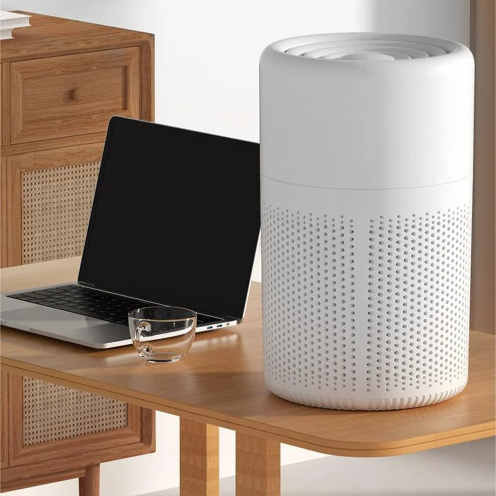 White cylindrical air purifier on a wooden desk with a laptop and glass.