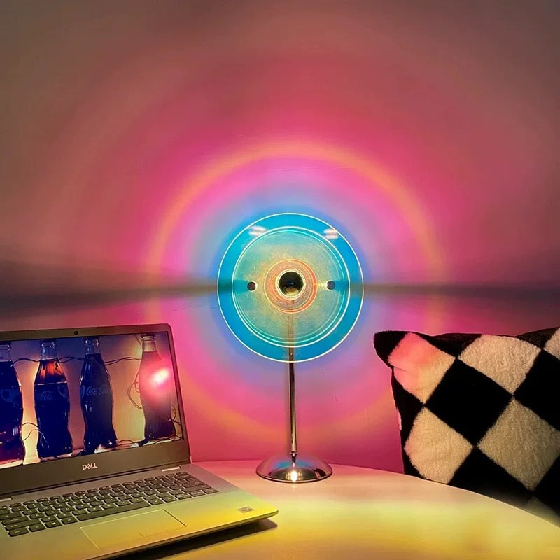 Colorful circular light projector on a desk with a laptop and pillow in the background