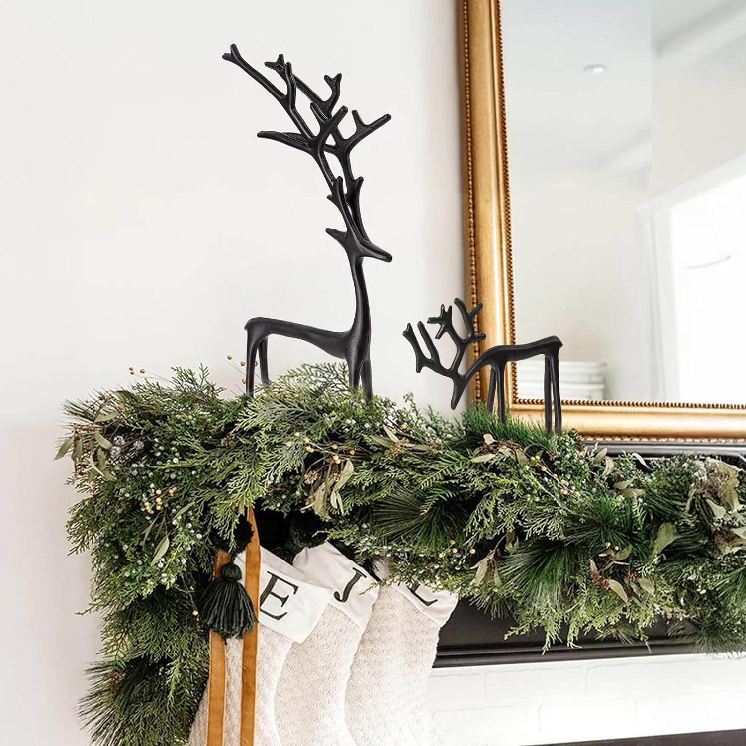 Decorative greenery with black deer antlers on a white wall with a gold-framed mirror.