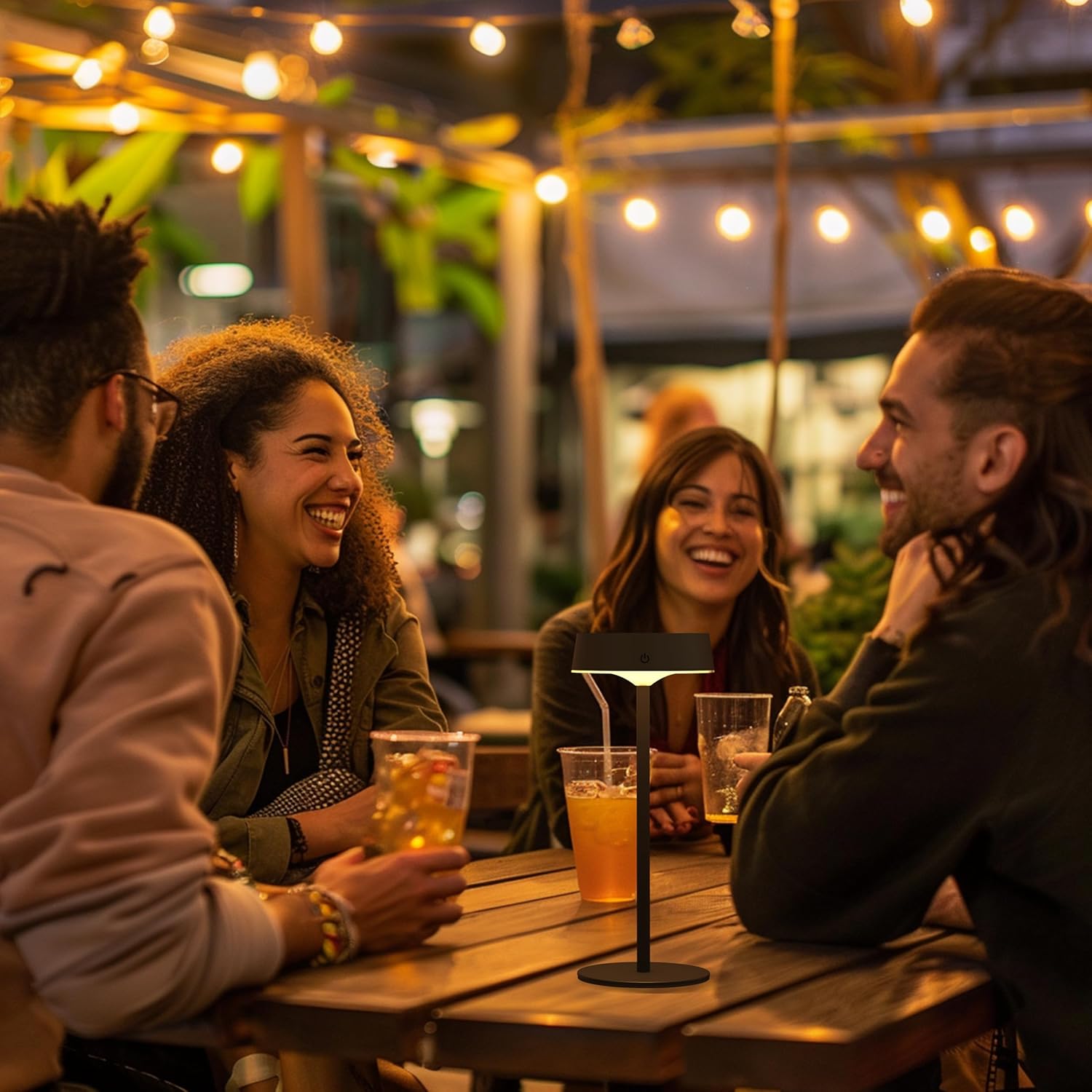 People enjoying drinks together at an outdoor bar with string lights and greenery.