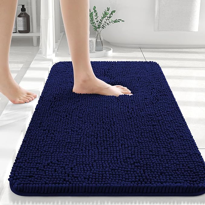 Navy blue bath mat on a bathroom floor with a person stepping onto it.