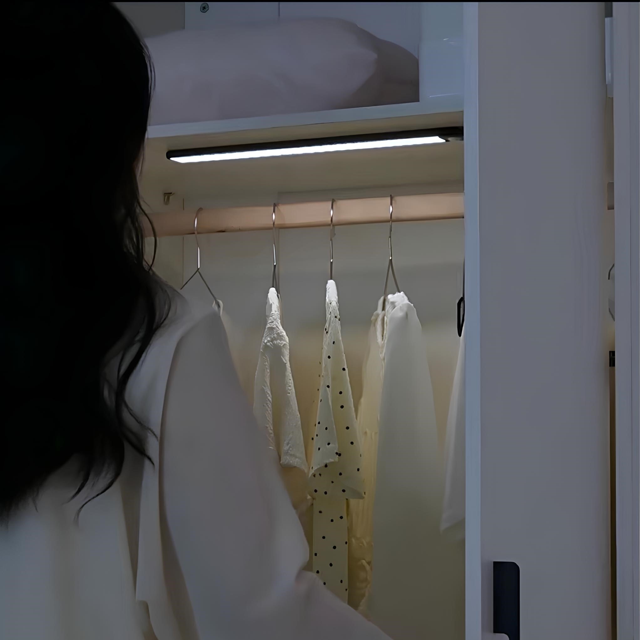 Person standing in front of a closet with clothes hanging on a rack.