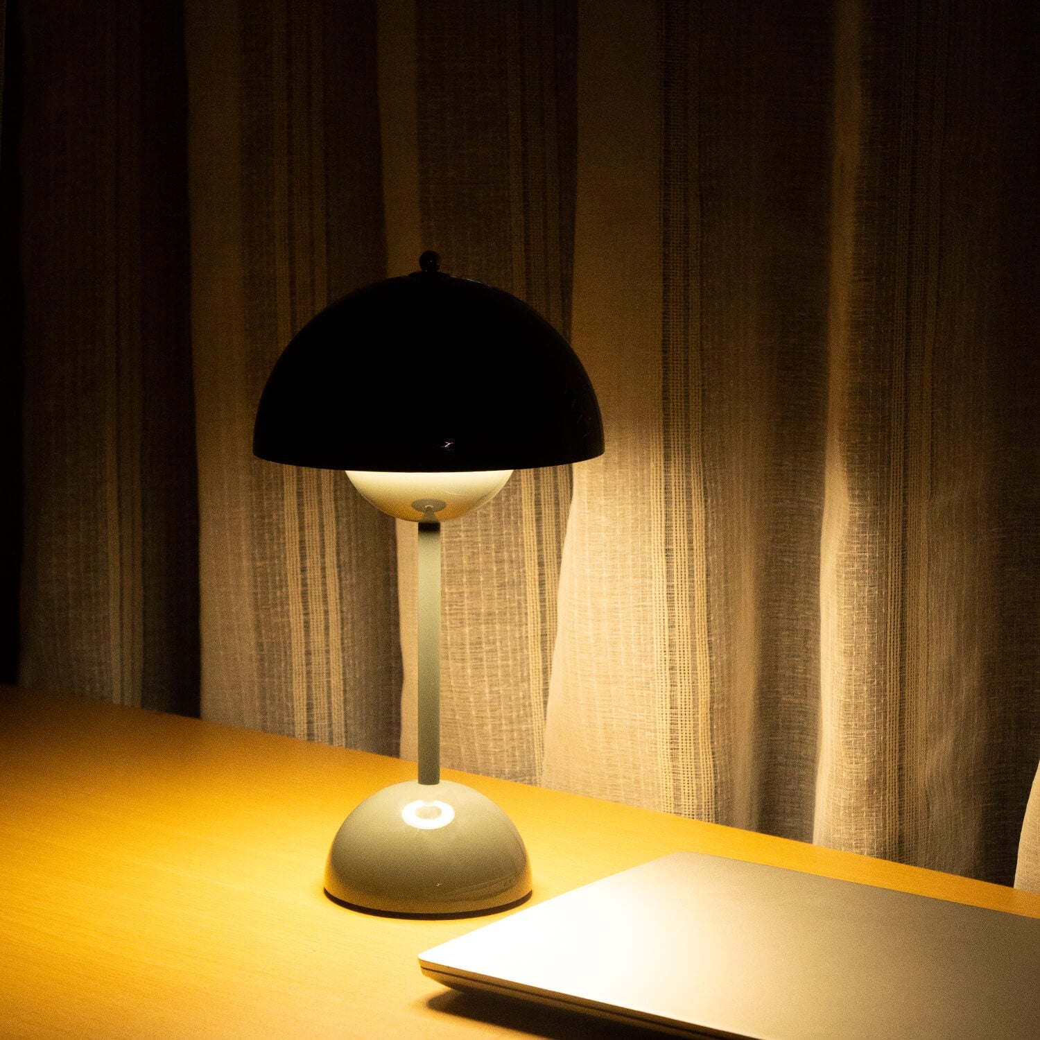 Table lamp on a desk with a warm glow in a dimly lit room.
