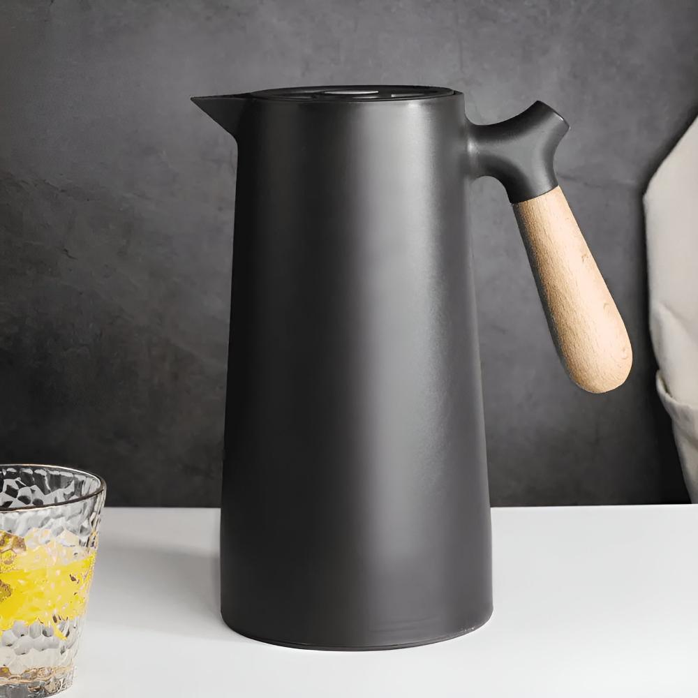 Black pitcher with a wooden handle on a white surface against a dark gray background