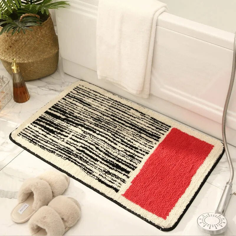 Decorative doormat with black and white pattern and red square on a floor next to a white door.