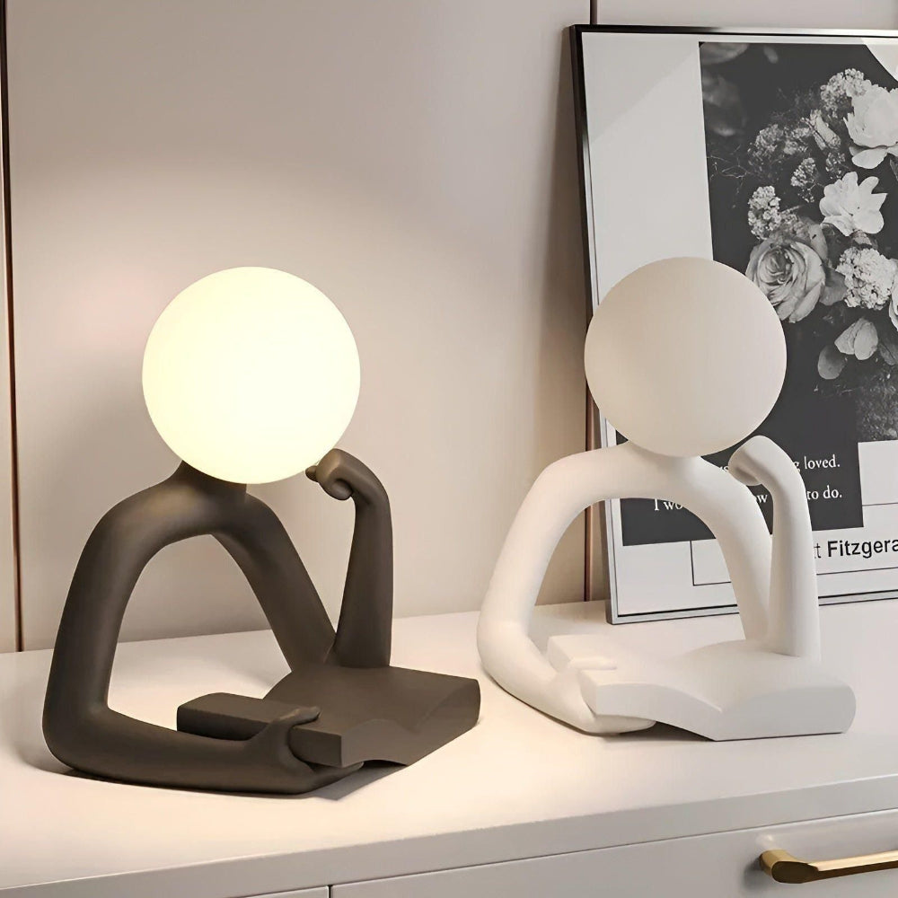 Two unique table lamps on a surface with a framed picture in the background.