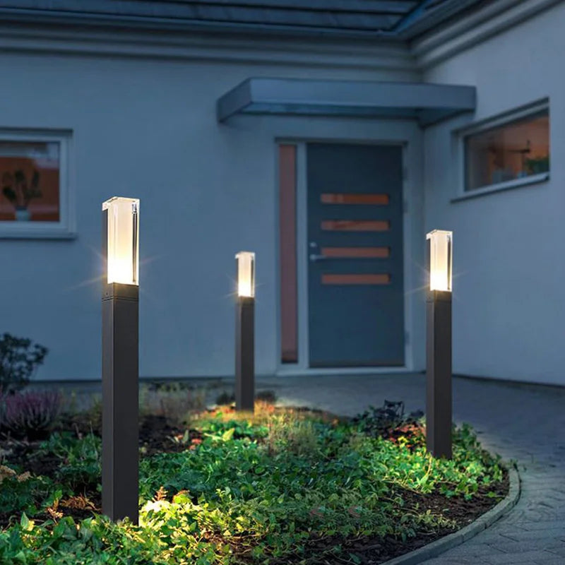 Three outdoor garden lights illuminating a pathway in front of a house.