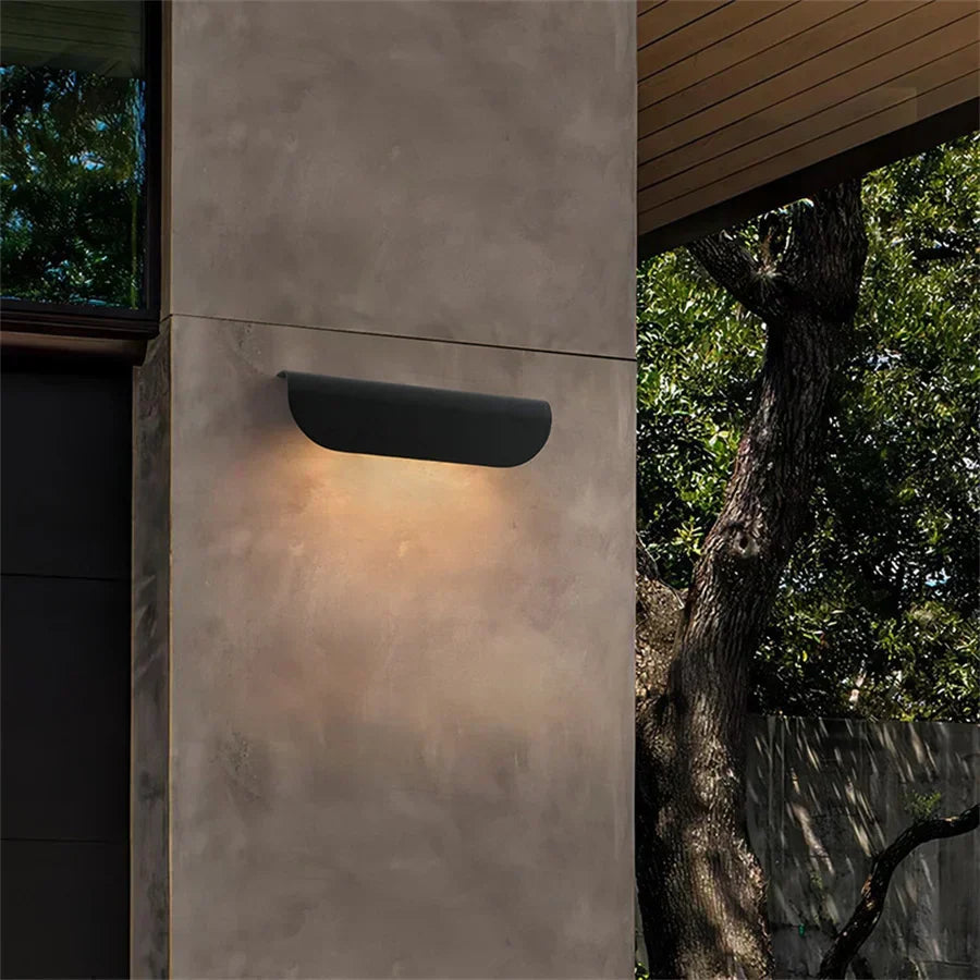 Wall-mounted outdoor light fixture on a concrete wall with natural background