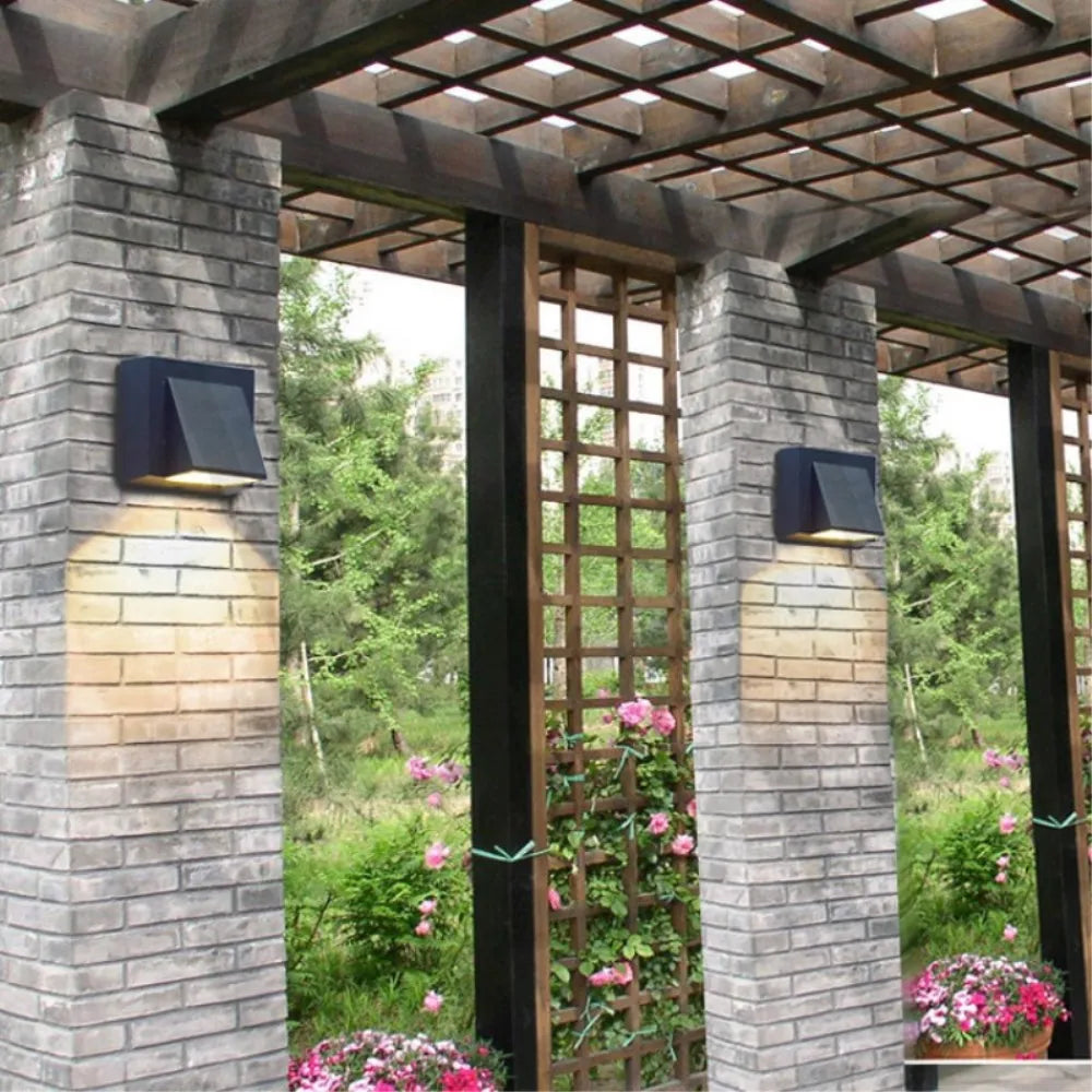 Outdoor setting with stone pillars, wall-mounted lights, and a trellis with greenery and flowers.