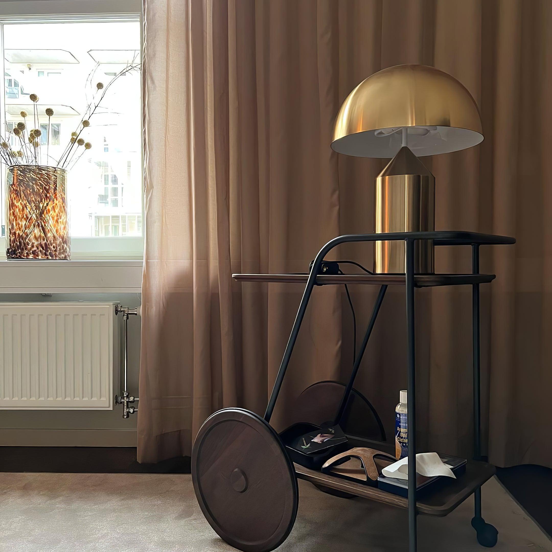 Modern bar cart with gold lamp against a window with pink curtains