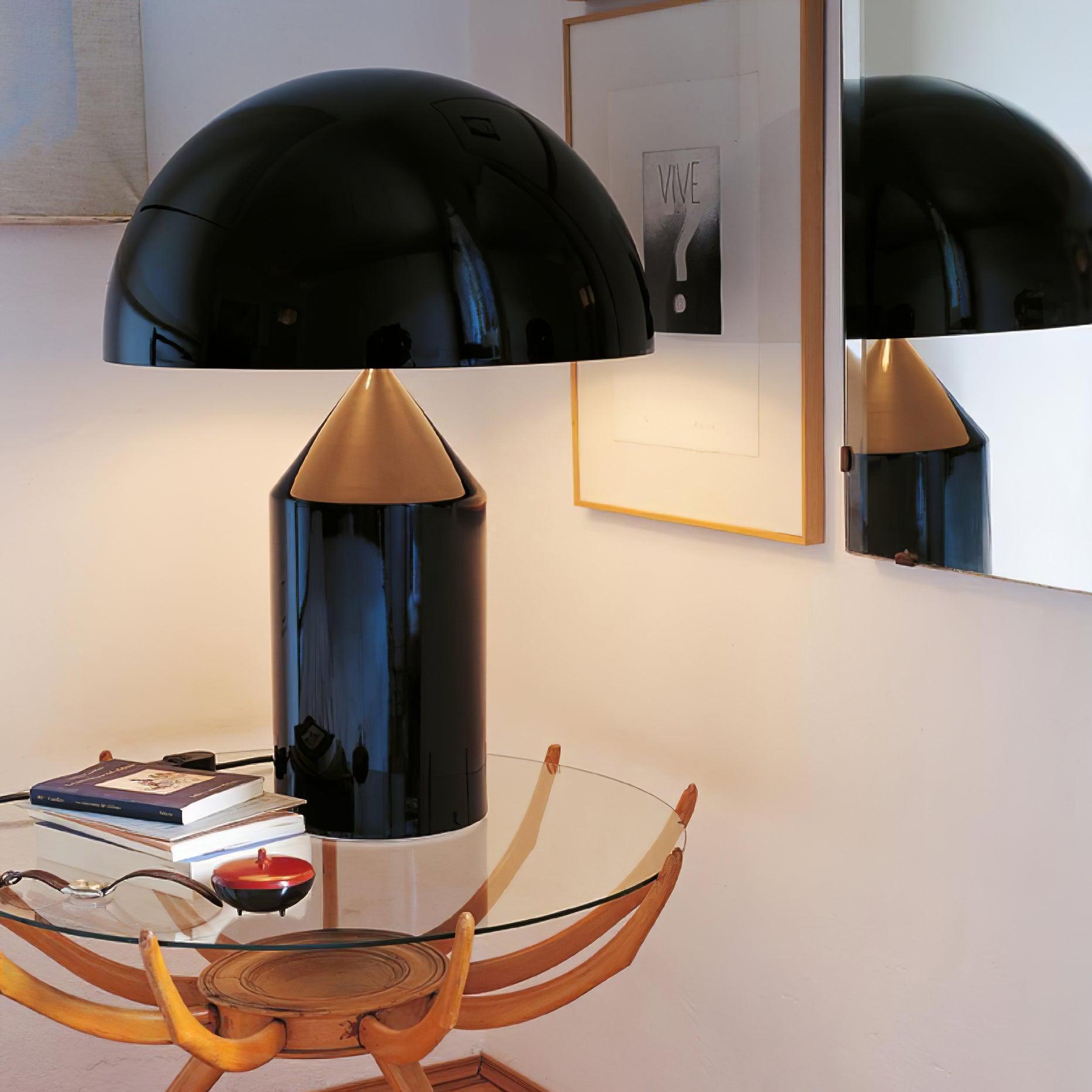 Modern black table lamp with gold accent on a glass table in a room setting.